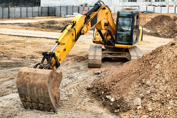 Chantier de terrassement en extérieur au coucher du soleil avec pelleteuse hydraulique sur chenilles rouge et noire en activité